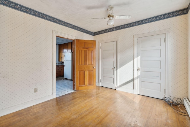 unfurnished bedroom with light wood-type flooring, white refrigerator, and ceiling fan