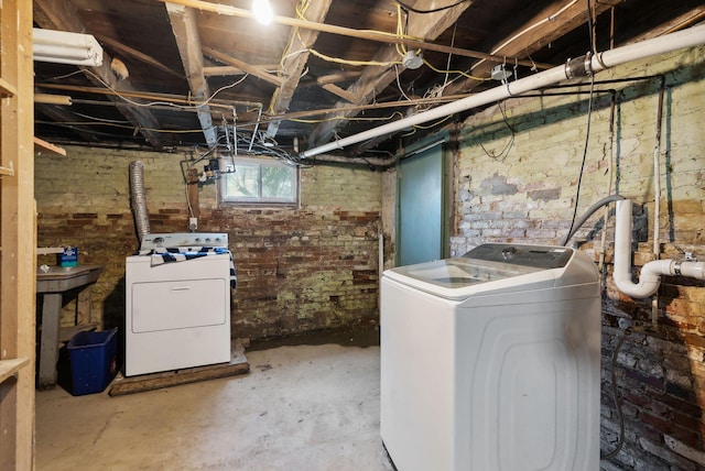 basement featuring washing machine and clothes dryer and brick wall