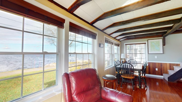 dining room featuring lofted ceiling with beams, a water view, wooden walls, and hardwood / wood-style flooring