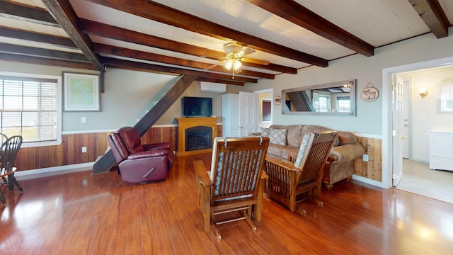 living room featuring an AC wall unit, wood walls, hardwood / wood-style flooring, beamed ceiling, and ceiling fan