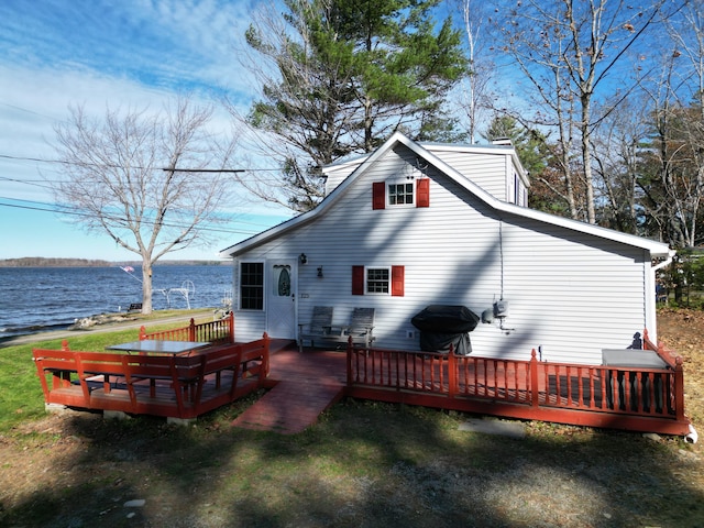 rear view of house with a deck with water view and a lawn