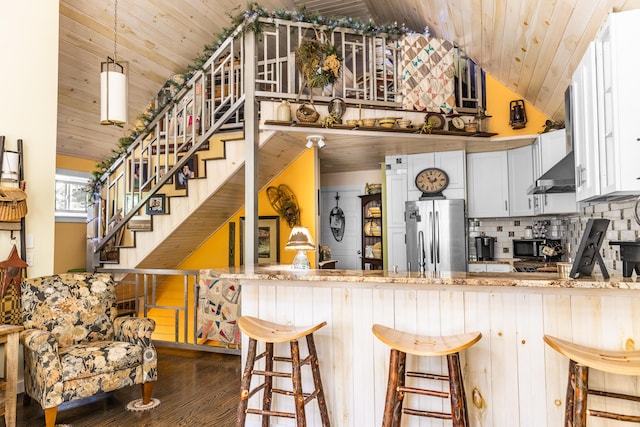 kitchen with kitchen peninsula, a breakfast bar area, decorative light fixtures, dark wood-type flooring, and stainless steel fridge