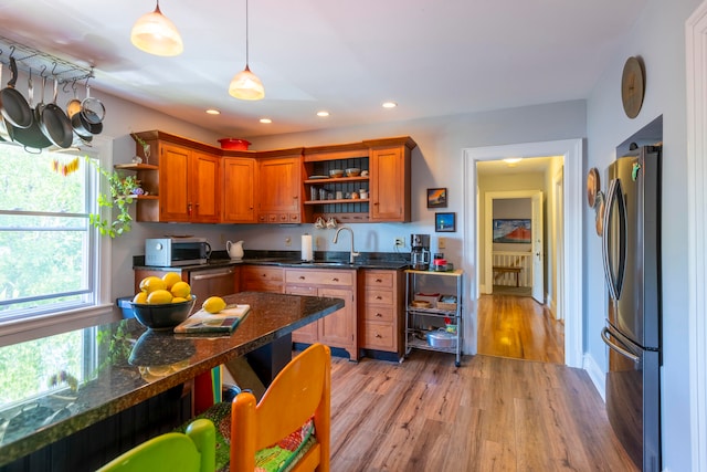 kitchen featuring stainless steel appliances, dark stone counters, sink, light hardwood / wood-style flooring, and decorative light fixtures