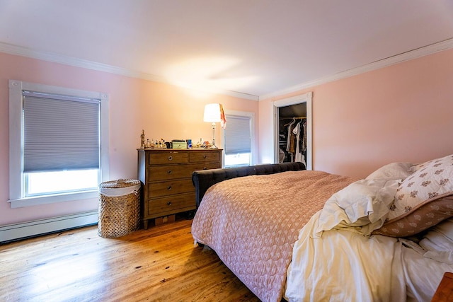 bedroom featuring a walk in closet, ornamental molding, wood-type flooring, a baseboard radiator, and a closet