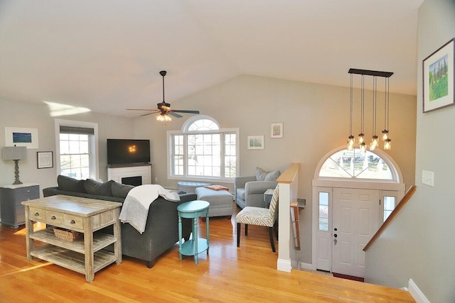 living room with a brick fireplace, ceiling fan, a wealth of natural light, and light hardwood / wood-style flooring