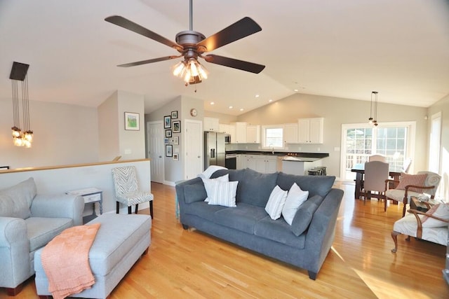 living room with ceiling fan with notable chandelier, light hardwood / wood-style floors, and vaulted ceiling