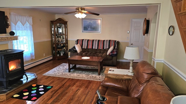 living room featuring baseboard heating, ceiling fan, a wood stove, crown molding, and dark wood-type flooring