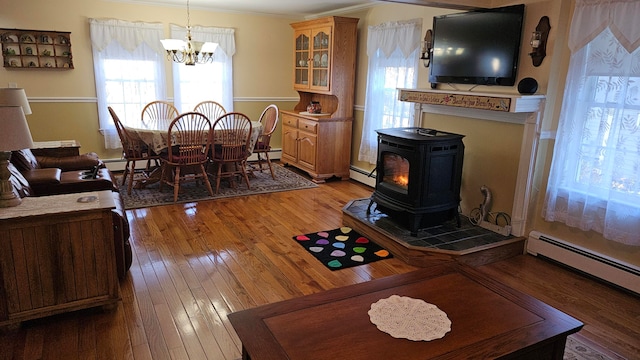 living room featuring ornamental molding, baseboard heating, wood-type flooring, a wood stove, and a notable chandelier