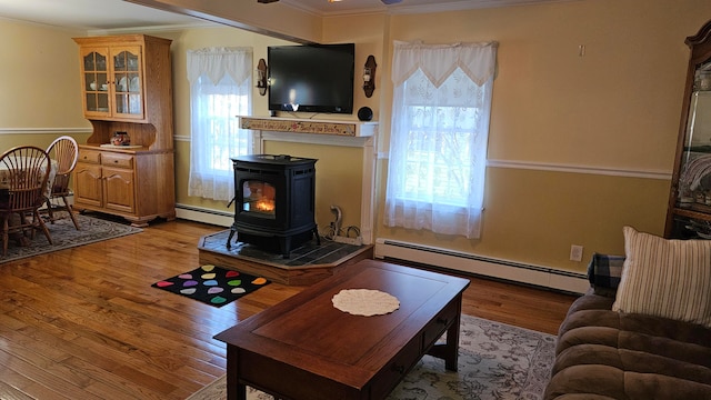 living room with a baseboard heating unit, light hardwood / wood-style floors, plenty of natural light, and a wood stove