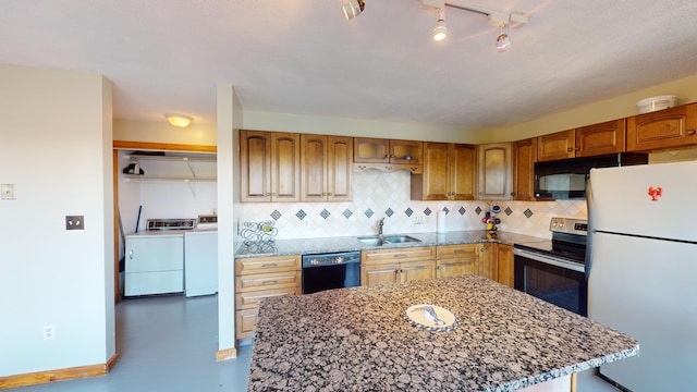 kitchen featuring black appliances, light stone counters, decorative backsplash, sink, and washing machine and dryer