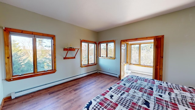 bedroom with multiple windows, hardwood / wood-style flooring, and a baseboard heating unit