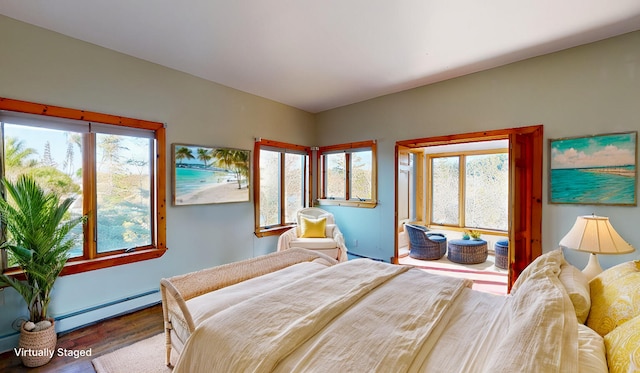 bedroom with multiple windows, hardwood / wood-style floors, and a baseboard heating unit