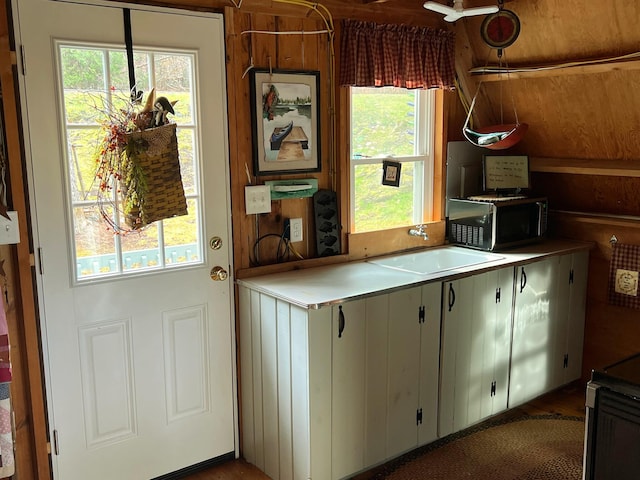 kitchen with stove, sink, white cabinetry, and wood walls