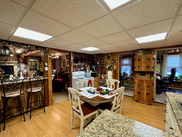 dining area featuring a paneled ceiling, wooden walls, bar, light hardwood / wood-style floors, and washing machine and dryer