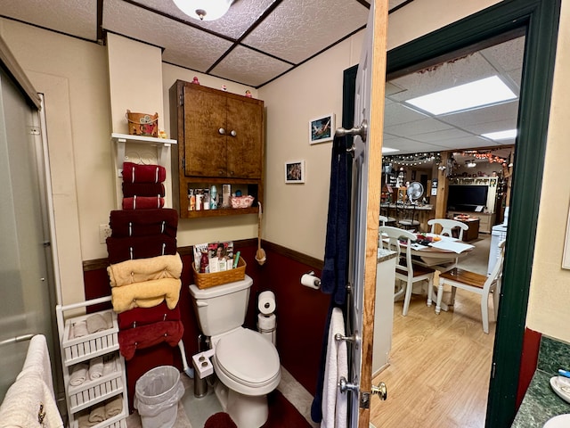 bathroom with a drop ceiling, wood-type flooring, and toilet