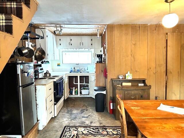 kitchen with stainless steel fridge, white electric range oven, wooden walls, pendant lighting, and white cabinets