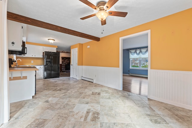 kitchen with beamed ceiling, black fridge, baseboard heating, and white cabinets