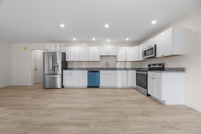 kitchen with dark stone counters, appliances with stainless steel finishes, sink, light hardwood / wood-style floors, and white cabinets