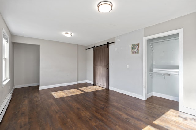 unfurnished bedroom featuring a barn door, dark hardwood / wood-style floors, baseboard heating, and a closet