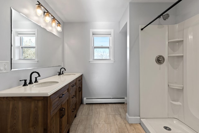 bathroom with walk in shower, vanity, baseboard heating, and a healthy amount of sunlight