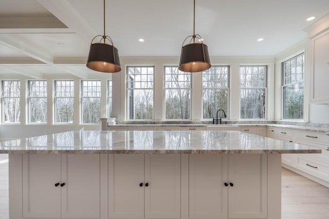 kitchen featuring white cabinets, light wood-type flooring, pendant lighting, and light stone counters