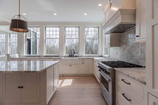 kitchen with high end range, light stone counters, ornamental molding, and custom exhaust hood