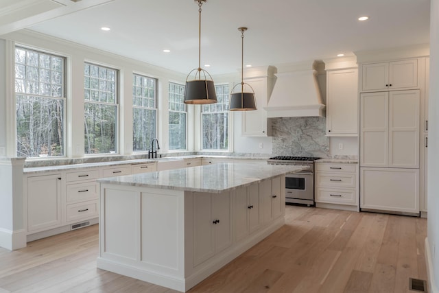 kitchen featuring custom exhaust hood, a kitchen island, white cabinets, stainless steel stove, and light wood-type flooring