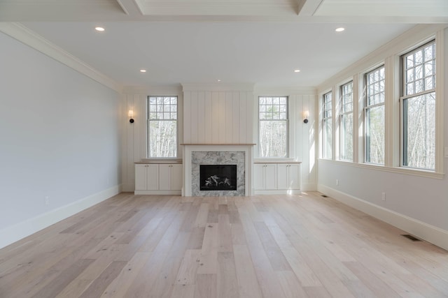 unfurnished living room with light wood-type flooring, a high end fireplace, crown molding, and plenty of natural light