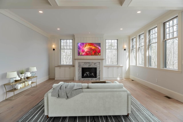 living room featuring light wood-type flooring, beam ceiling, a premium fireplace, and crown molding