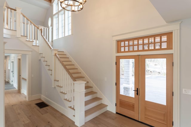 entryway featuring an inviting chandelier, french doors, light hardwood / wood-style floors, and a towering ceiling