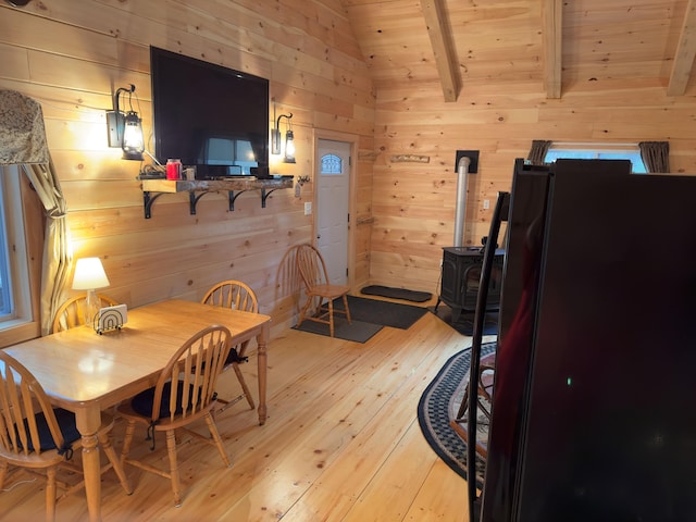 dining area with wooden ceiling, a wood stove, wooden walls, light wood-type flooring, and lofted ceiling with beams