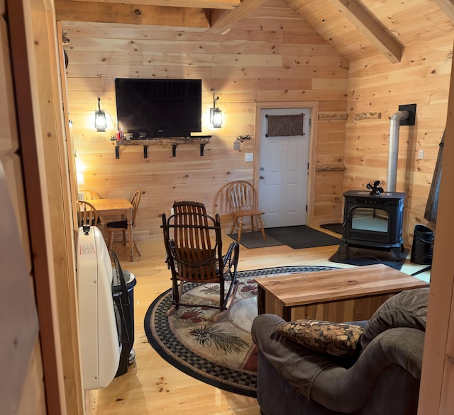 living room with light wood-type flooring, wood walls, a wood stove, and vaulted ceiling with beams