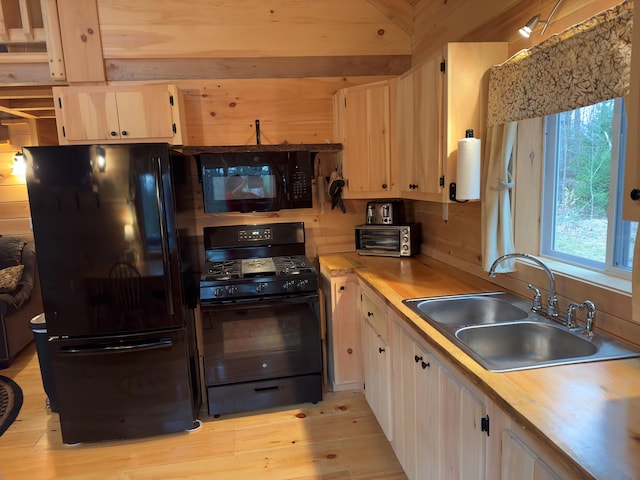 kitchen with sink, black appliances, beam ceiling, wooden walls, and light wood-type flooring