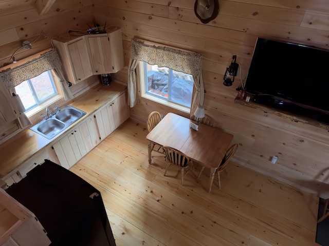 kitchen with white cabinetry, wooden walls, sink, and light hardwood / wood-style flooring