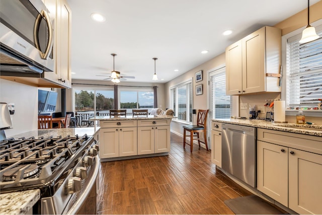 kitchen with dark wood-type flooring, decorative light fixtures, cream cabinetry, and stainless steel appliances