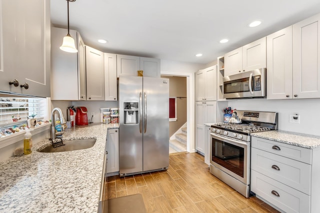 kitchen with stainless steel appliances, light hardwood / wood-style floors, sink, light stone countertops, and decorative light fixtures