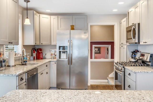 kitchen with wood-type flooring, light stone counters, appliances with stainless steel finishes, decorative light fixtures, and sink