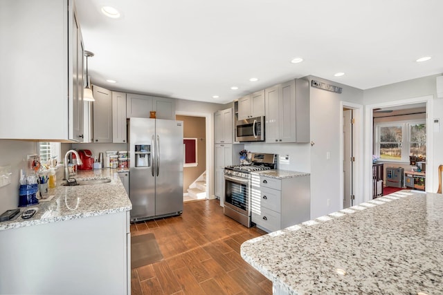 kitchen featuring gray cabinetry, light stone counters, appliances with stainless steel finishes, sink, and dark wood-type flooring