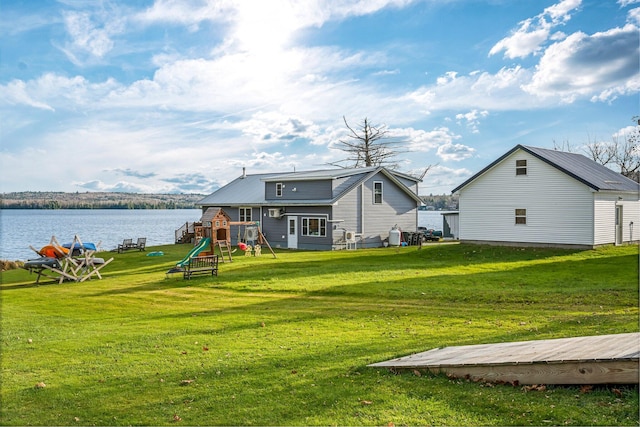 rear view of property featuring a playground, a water view, and a yard