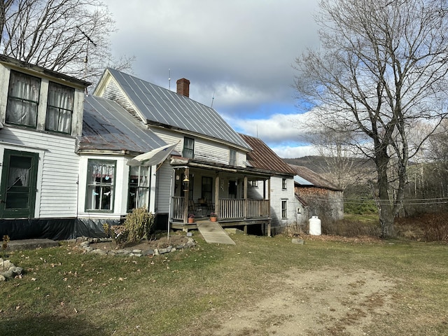 rear view of property featuring solar panels, a lawn, a chimney, metal roof, and covered porch