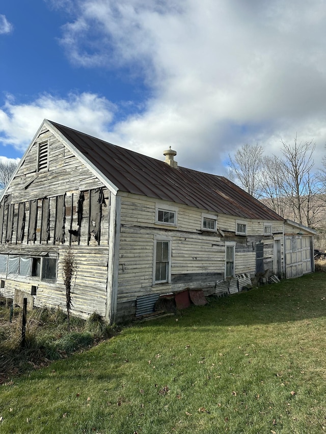 back of house featuring metal roof, a yard, a chimney, and a standing seam roof