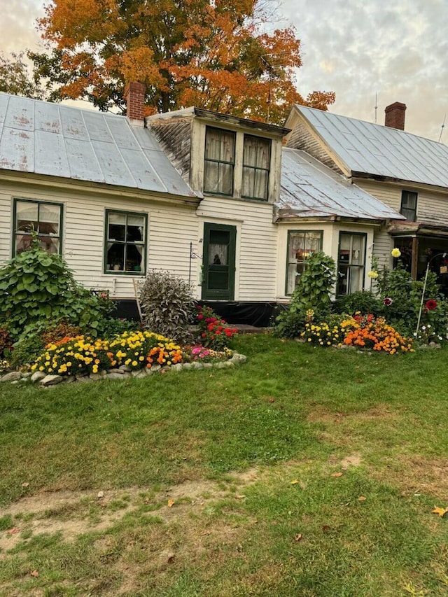 rear view of house featuring a standing seam roof, metal roof, a chimney, and a lawn