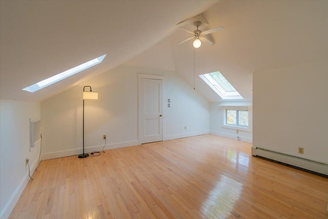 additional living space featuring vaulted ceiling with skylight, light wood-type flooring, and a baseboard heating unit