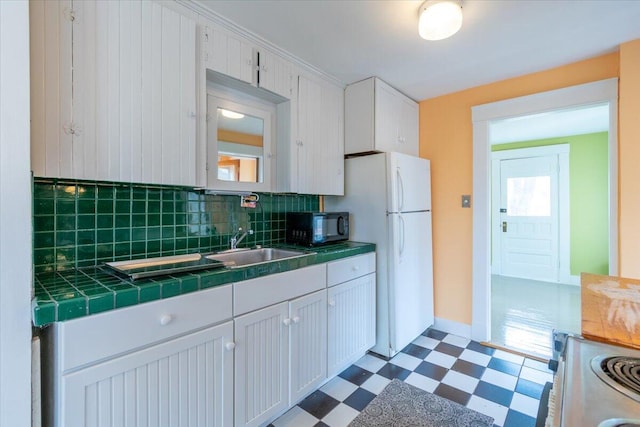 kitchen with tile counters, white cabinets, decorative backsplash, stove, and white fridge