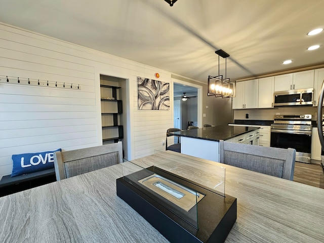 kitchen featuring stainless steel appliances, wood-type flooring, white cabinetry, hanging light fixtures, and wood walls