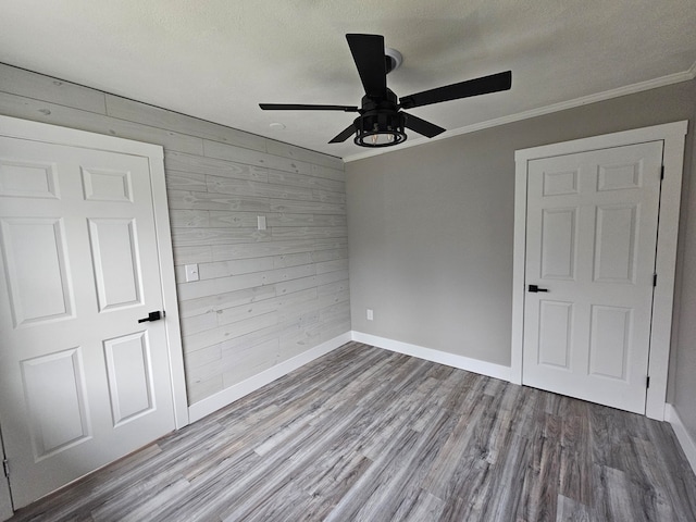 unfurnished bedroom featuring wooden walls, ceiling fan, light wood-type flooring, a textured ceiling, and ornamental molding