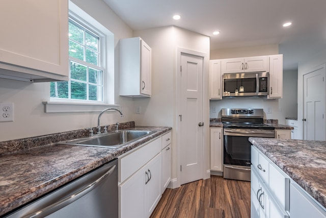 kitchen featuring appliances with stainless steel finishes, dark hardwood / wood-style flooring, sink, dark stone countertops, and white cabinetry