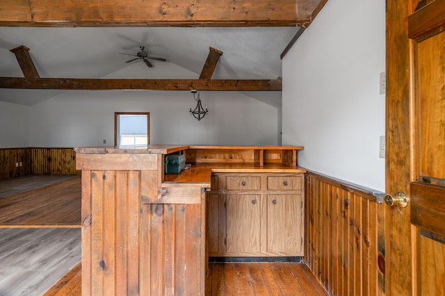 kitchen featuring ceiling fan, vaulted ceiling with beams, light hardwood / wood-style flooring, wooden walls, and pendant lighting