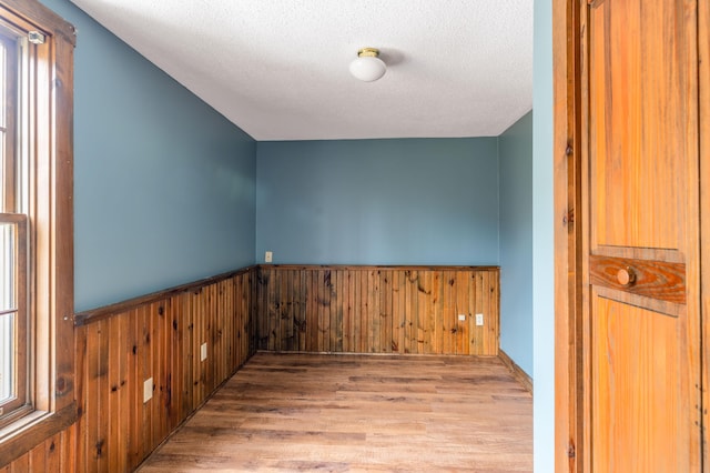 additional living space with wood walls, light wood-type flooring, and a textured ceiling