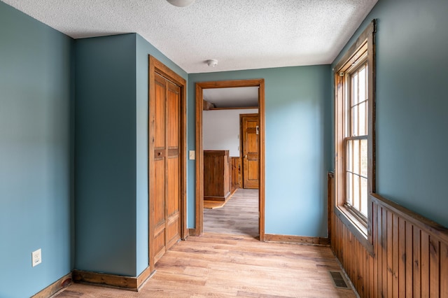 hallway with a textured ceiling and light hardwood / wood-style flooring